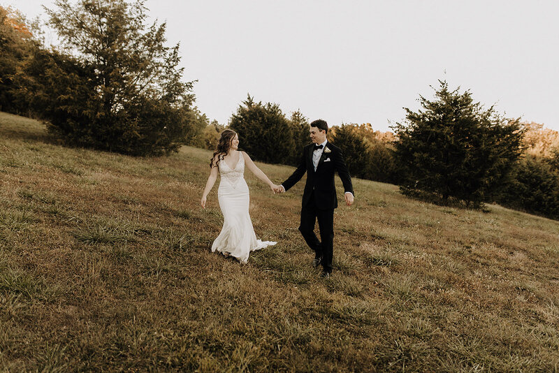 Bride and groom holding hands and walking in a field