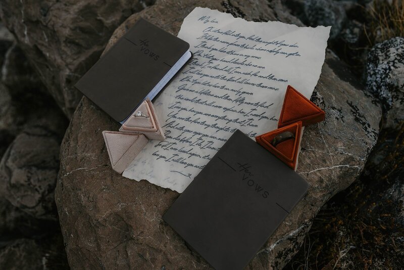 Two dark journals, a handwritten letter, and triangle-shaped items rest on a large rock outdoors—perfect details captured by an Ouray Colorado elopement photographer.