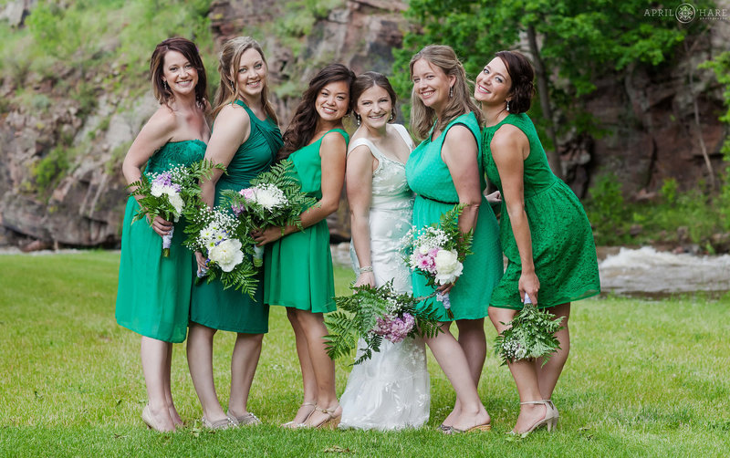 Bride poses for a cute photo with her bridesmaids all wearing jewel green dresses at Riverbend in Lyons Colorado