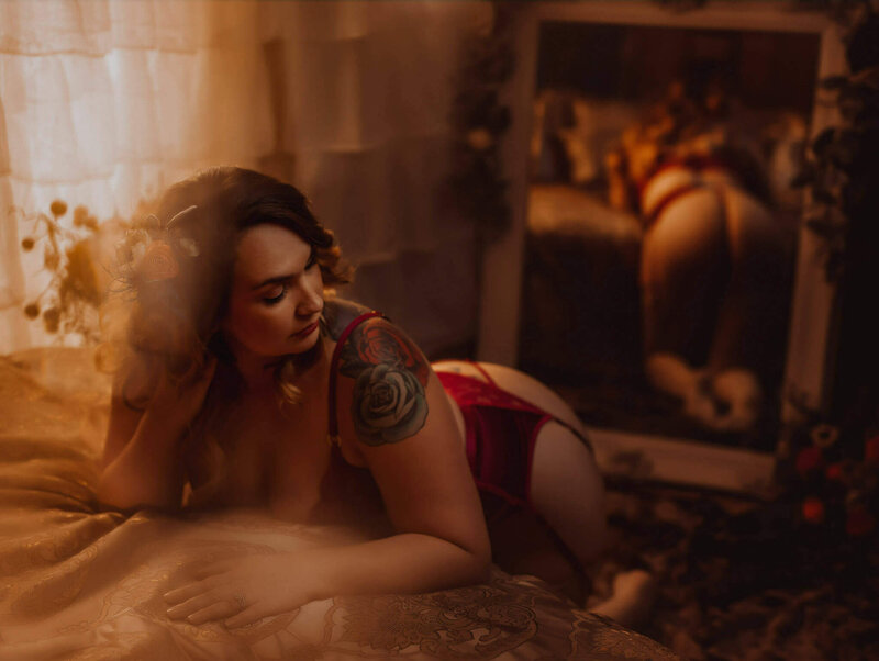 Woman with dark hair wearing red lingerie leaning on a bed in a DWF boudoir studio