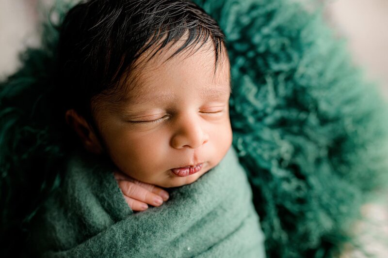 Close-up image of a baby's profile as he is wrapped in a teal green layer laying on a teal fur