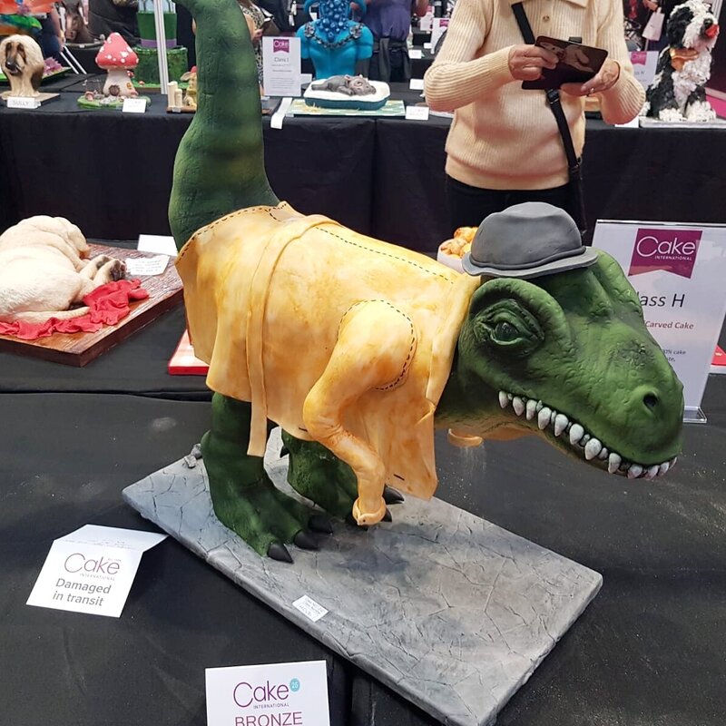 Fully standing, gravity-defying carved dinosaur cake in detective coat and hat