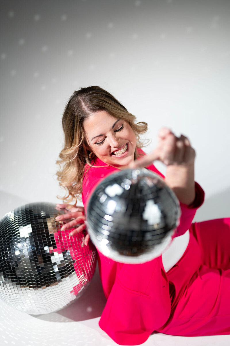 A woman sitting on the ground holding a disco ball with one hand.