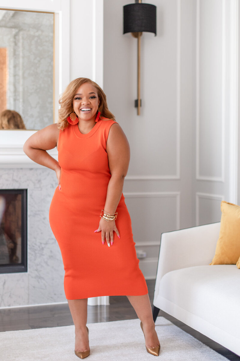 Digital Marketing coach smiling with hand on her hip in bright orange dress
