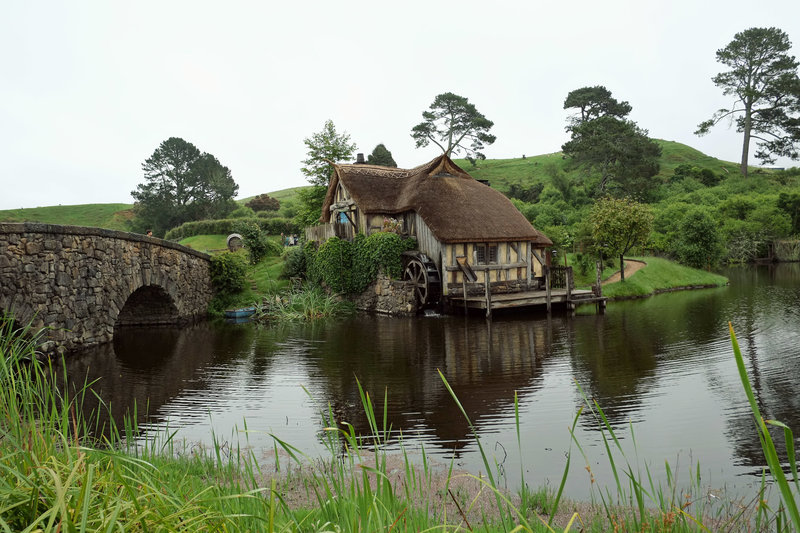 A photo from Hobbiton in New Zealand of a house on a small lake