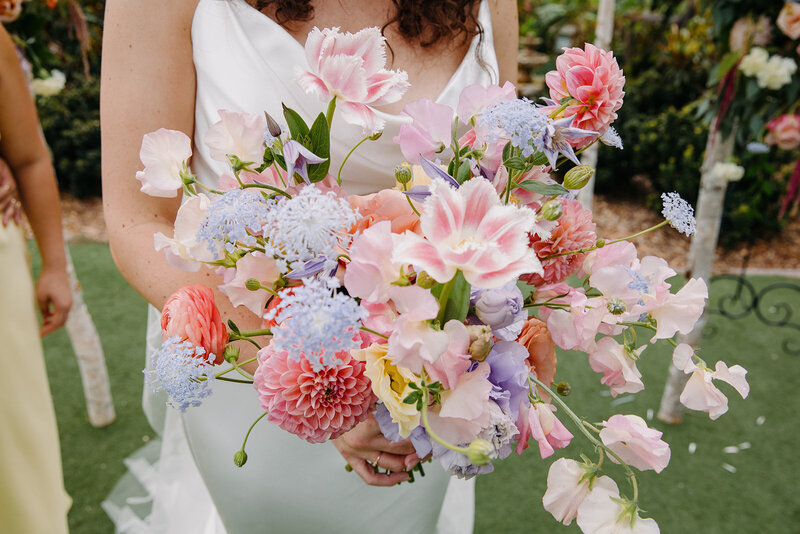 Bride holding a bouquet of pastel-toned flowers in an outdoor setting.