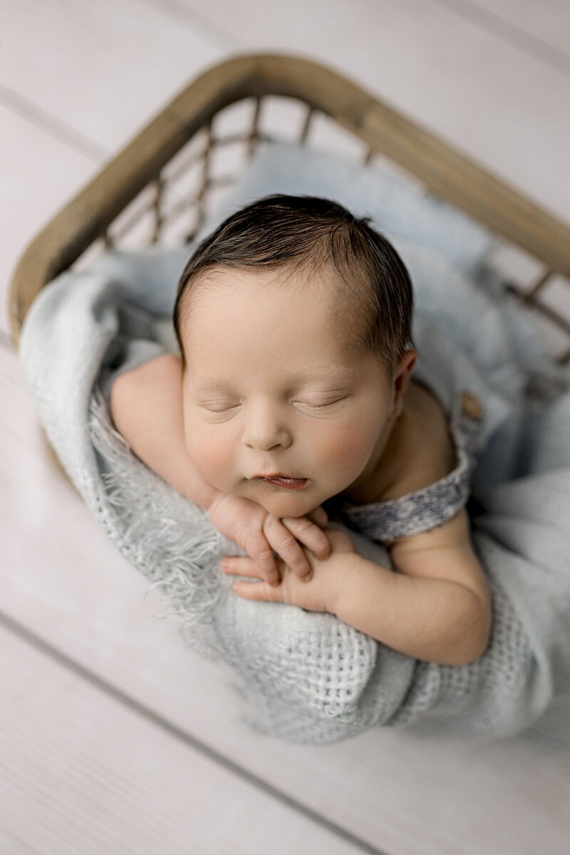 lifestyle newborn session posed baby image of newborn and crate pose gently with his hands under his cheek highlighting his head full of hair