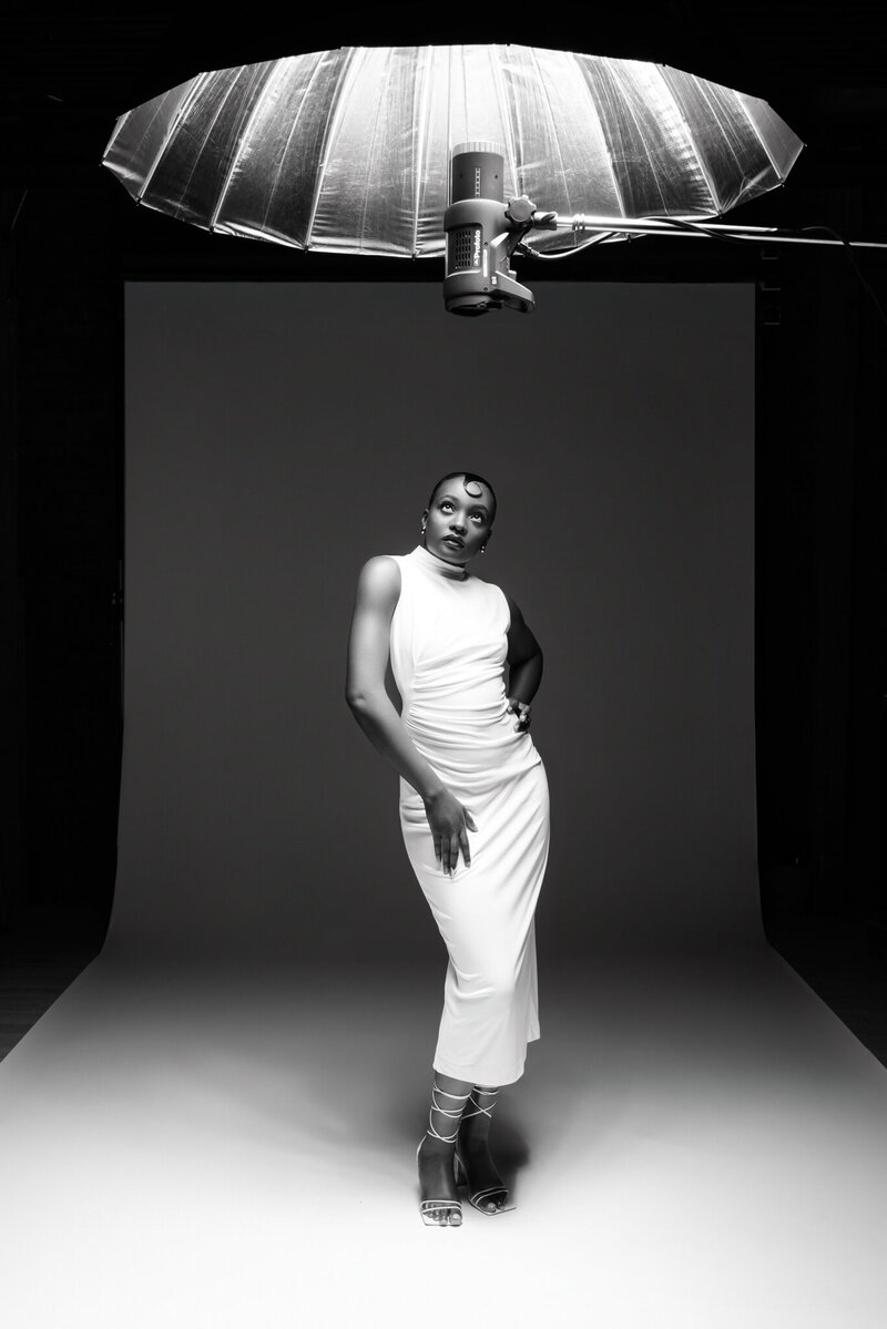 Editorial black and white branding portrait of Black woman in white gown under parabolic studio light at Tamara Hudson Studios
