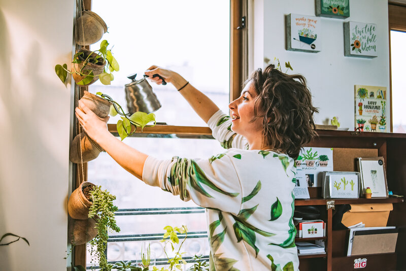 Woman waters her hanging plants in her apartment window