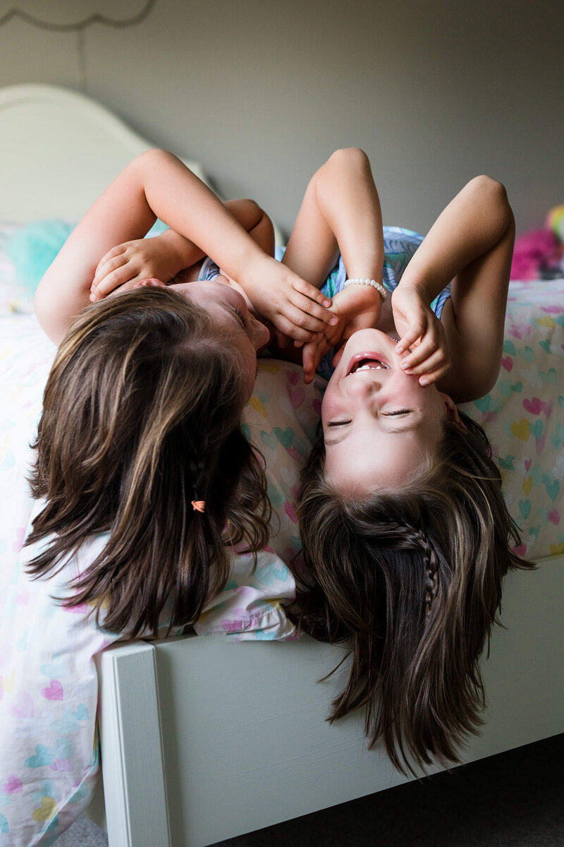 Two sisters laugh on bed in Edina, MN Family Photography Session