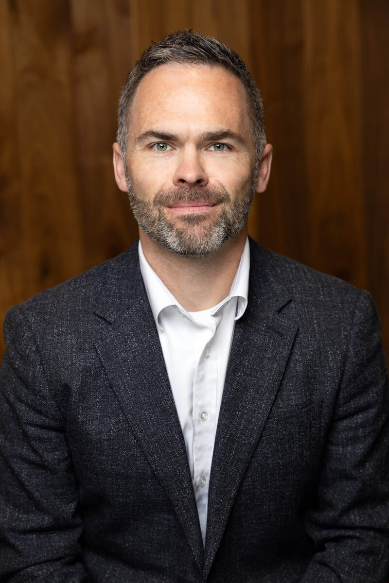Corporate headshot of man in gray suit with wood panel backdrop in Utah.