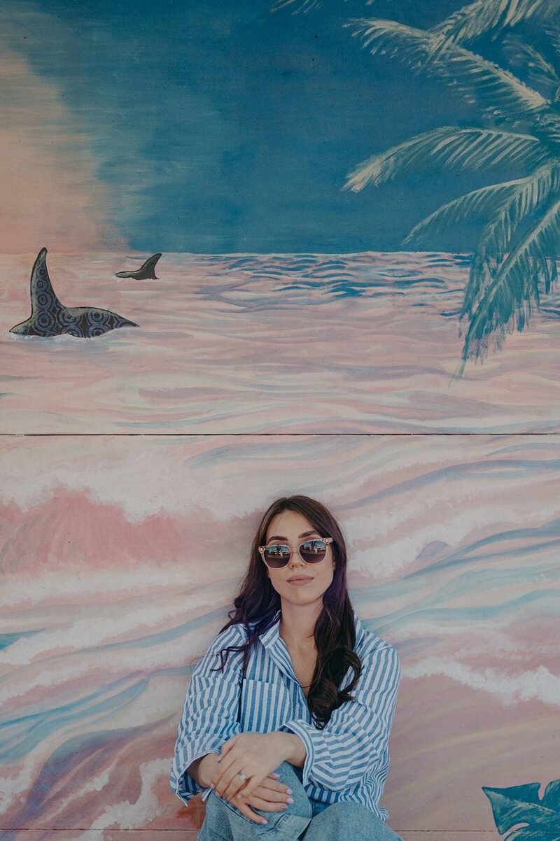 Creative branding portrait of Sharni Tolhurst sitting against a pastel ocean mural.