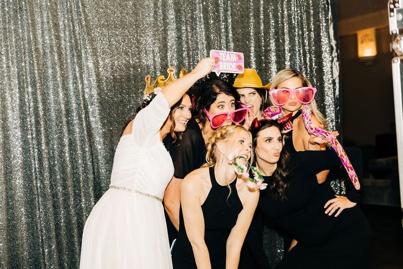 A group of women smiling and posing for a photo in a photo booth, capturing a joyful moment together.