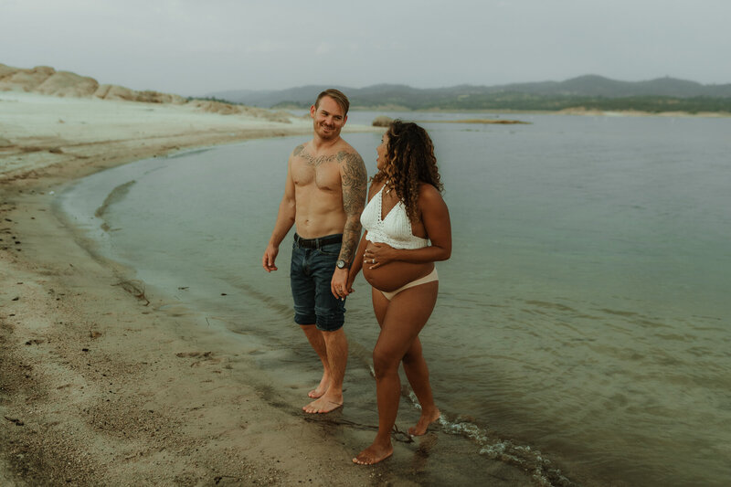 Pregnant mom walks on folsom beach holding her husband's hand.