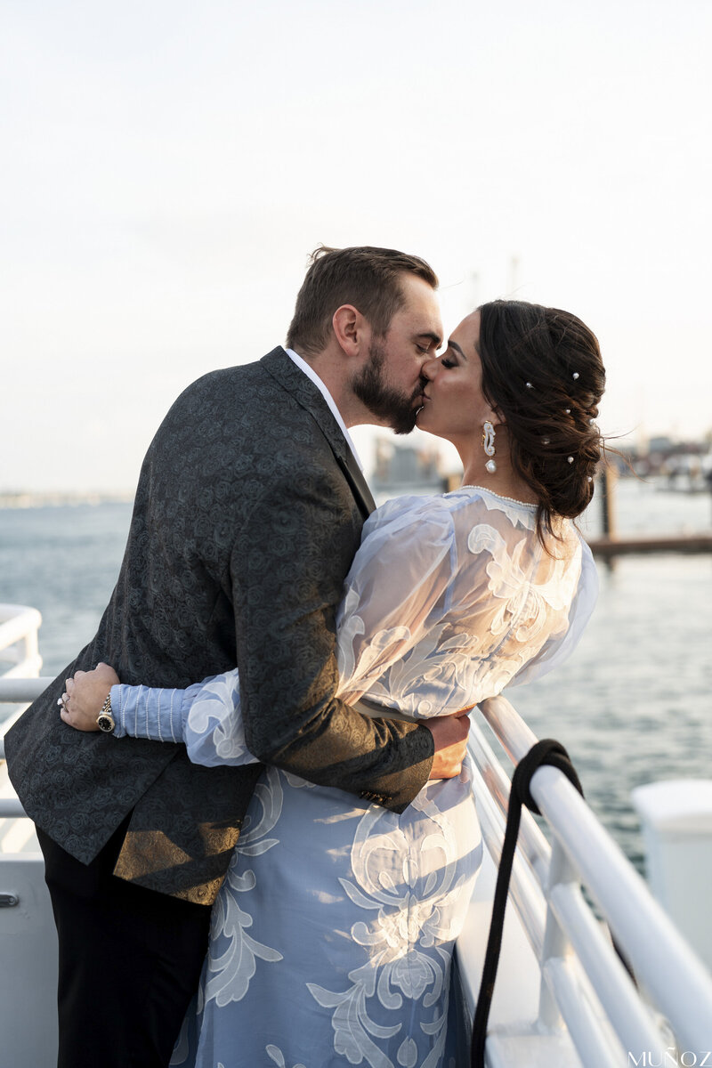 A couple shares a romantic kiss on a boat with an ocean backdrop, capturing the elegance and romance of a destination wedding by Socially Significant Events.