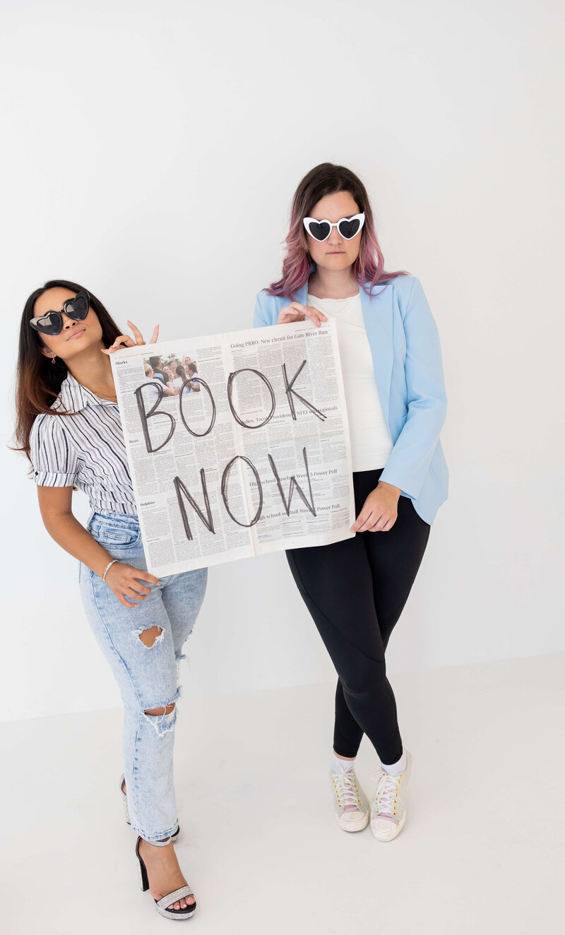 Woman team at Florida Social Butterfly in sunglasses and blue blazer with newspaper that says Book Now