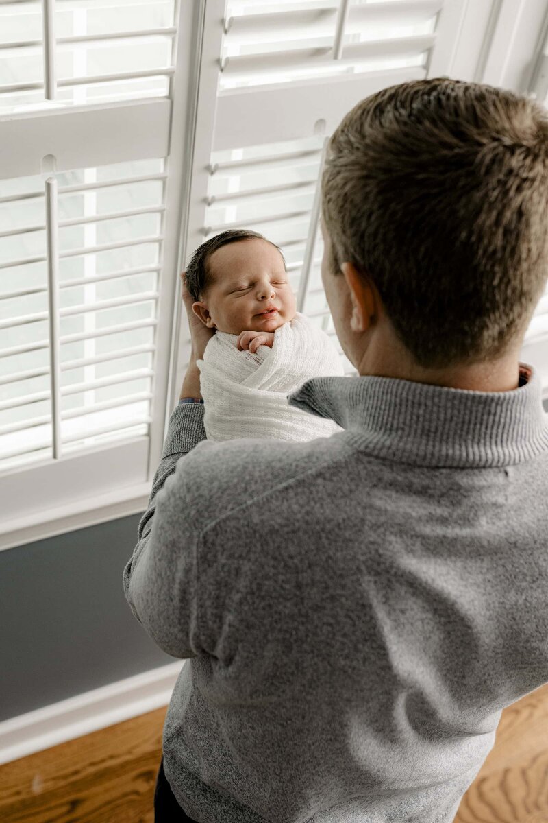 Overhead image of Father looking down towards his newborn son where you can see the baby's face and the back of Dad's head