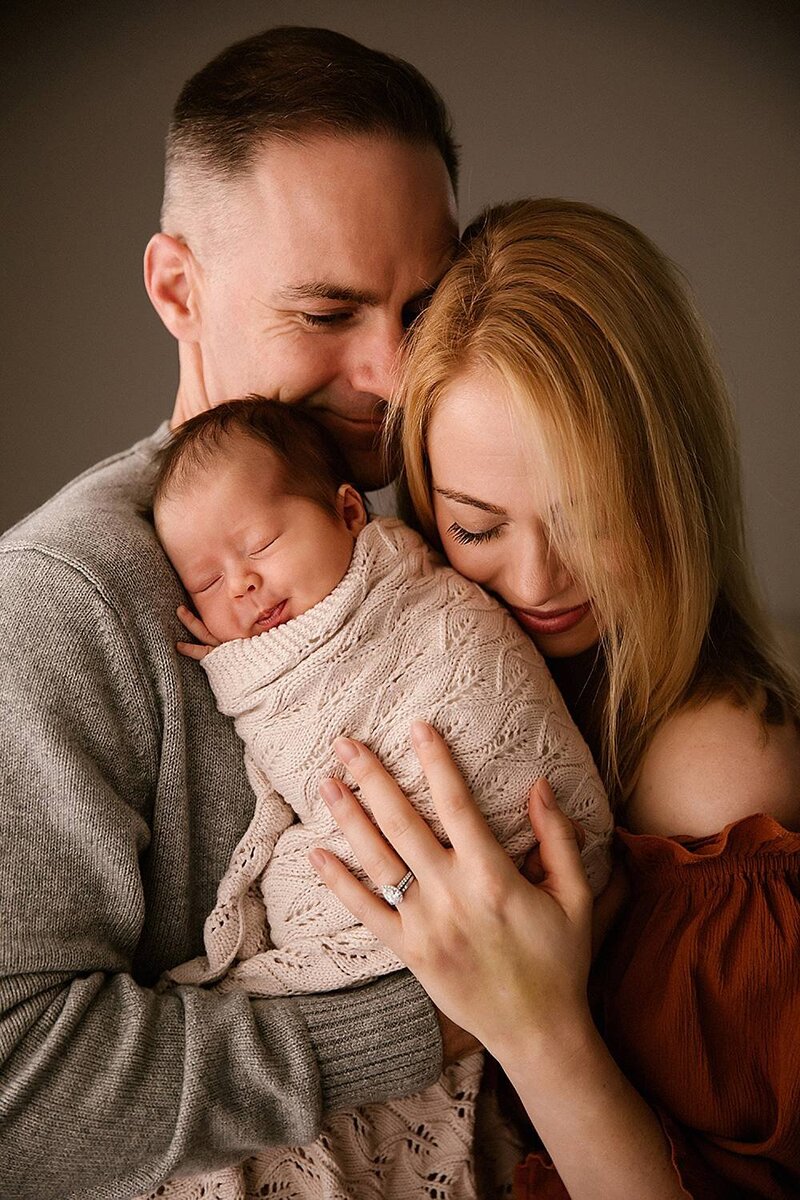 Megan and her husband holding their newborn baby during their photography session with Aimee Kelly Photography
