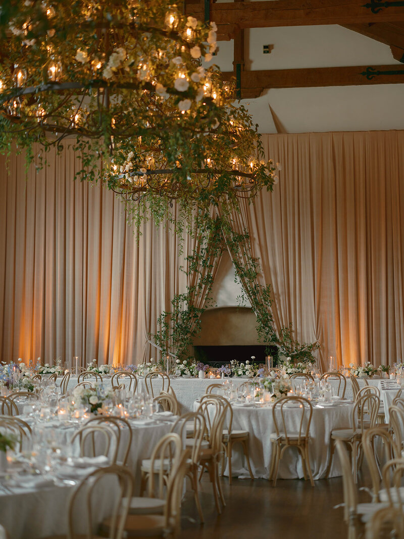 Wedding reception tables set up in an outdoor arched corridor overgrown with ivy