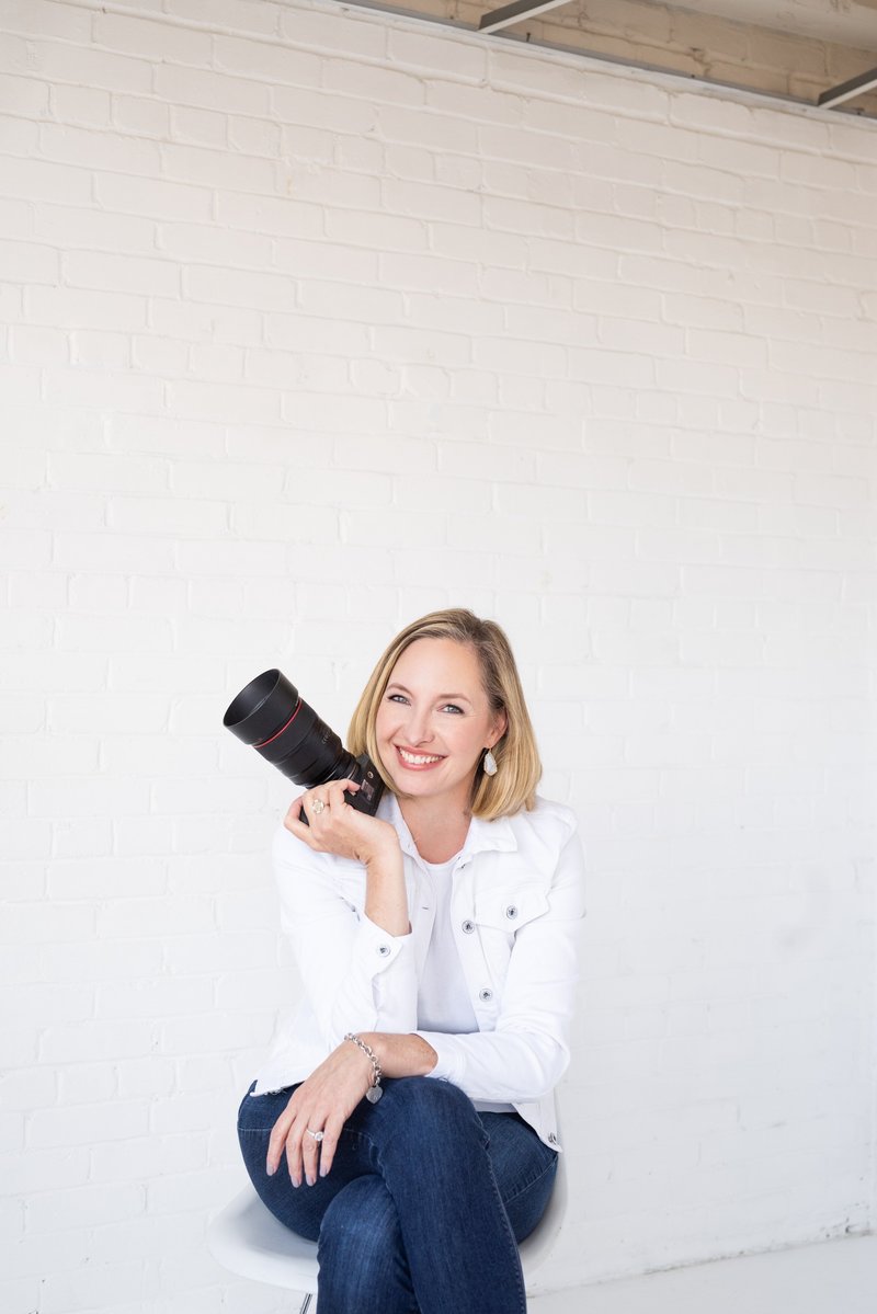 Jennifer Denton holding a camera sitting down in front of white wall