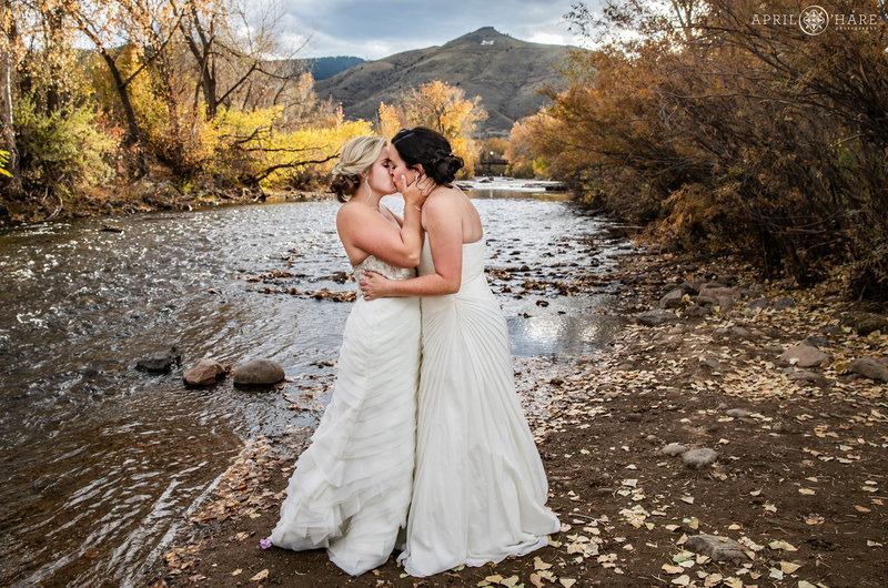 Brides kiss on their wedding day with Clear Creek in the backdrop in Golden Colorado