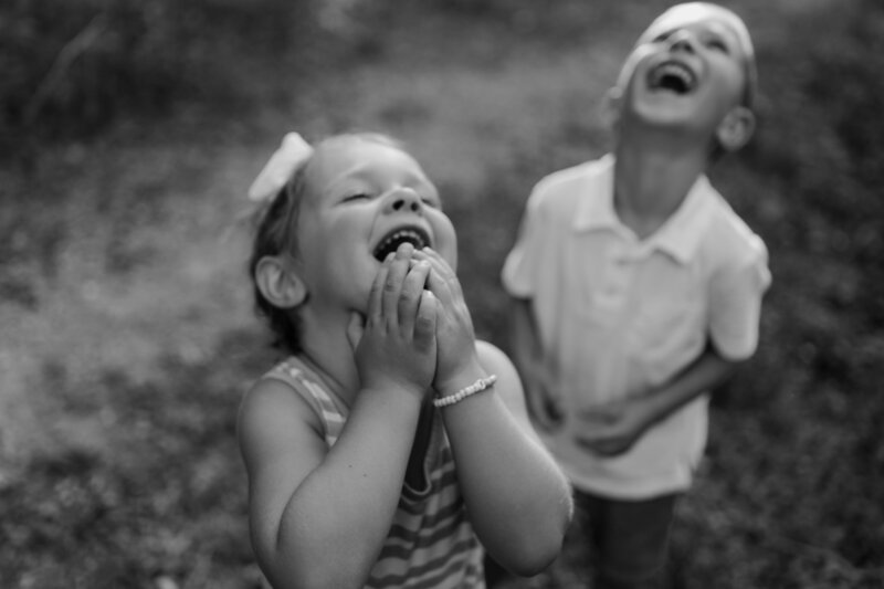 A young boy and young girl throw their heads back in laughter