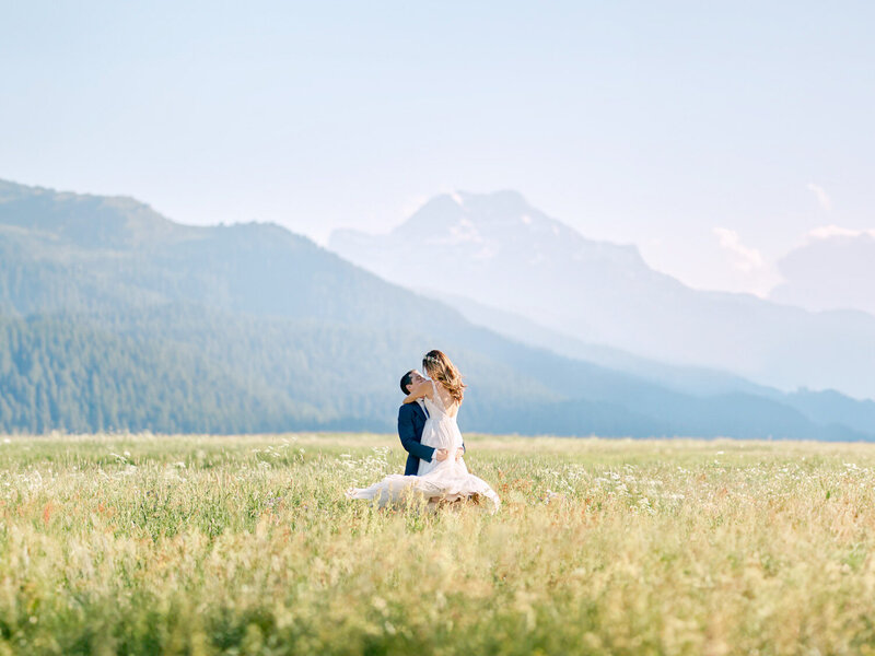 Bride and groom spinning in feild in front of mountains