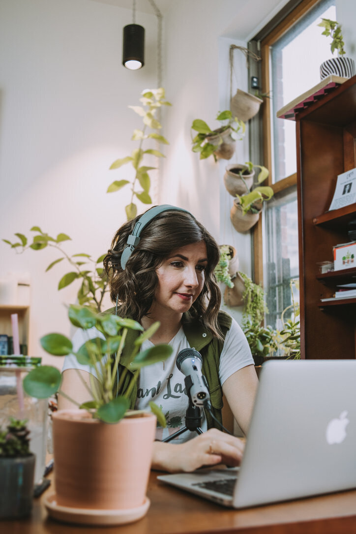 Woman sits on her laptop at her desk with plants surrounding her and Soltech grow light hanging from ceiling