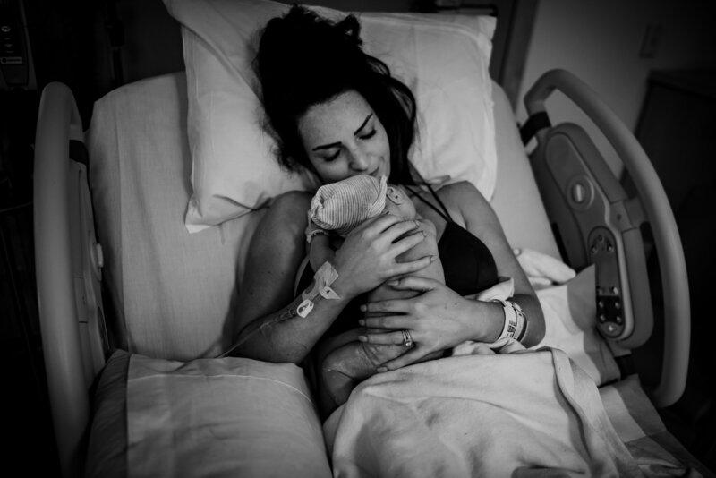 Black and white photo  of a woman lying in a hospital bed holding a newborn baby