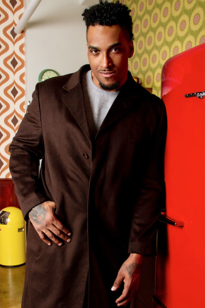 Personal branding portrait Joe Barksdale leaning against red refrigerator wearing dark brown overcoat