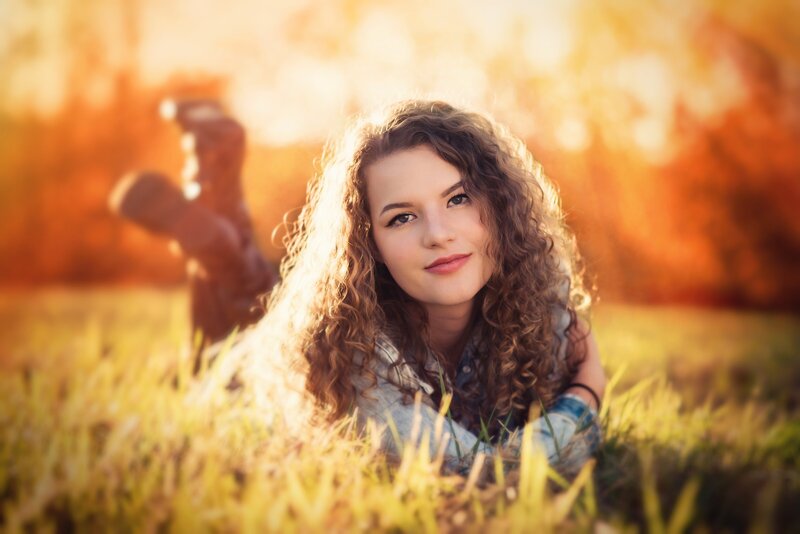 teen girl lays on her stomach in a field and smiles for senior portrait photograph