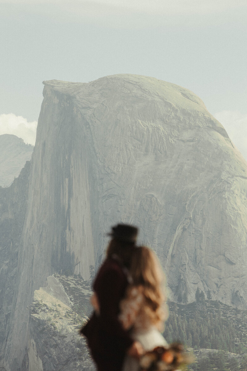 man and woman embracing as they look out at half dome in yosemite
