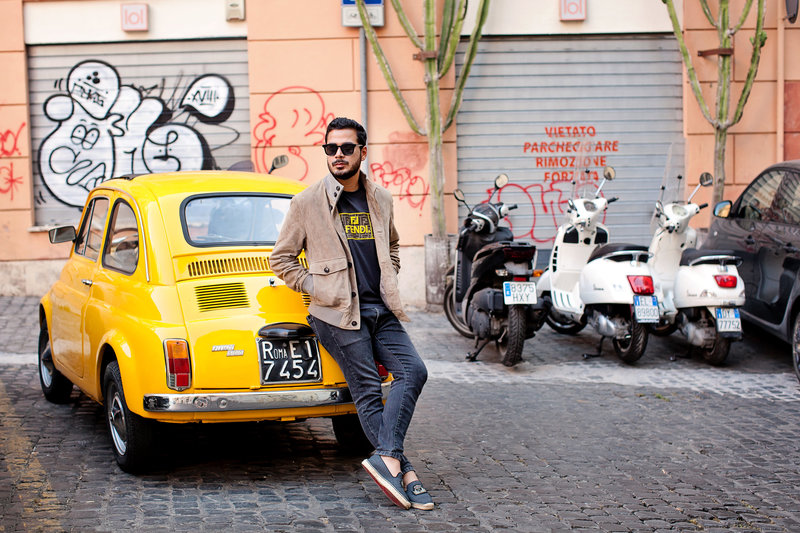 A guy leaning again a classic old yellow fiat in Monti. Taken by Rome Solo Travel Photographer, Tricia Anne Photography.