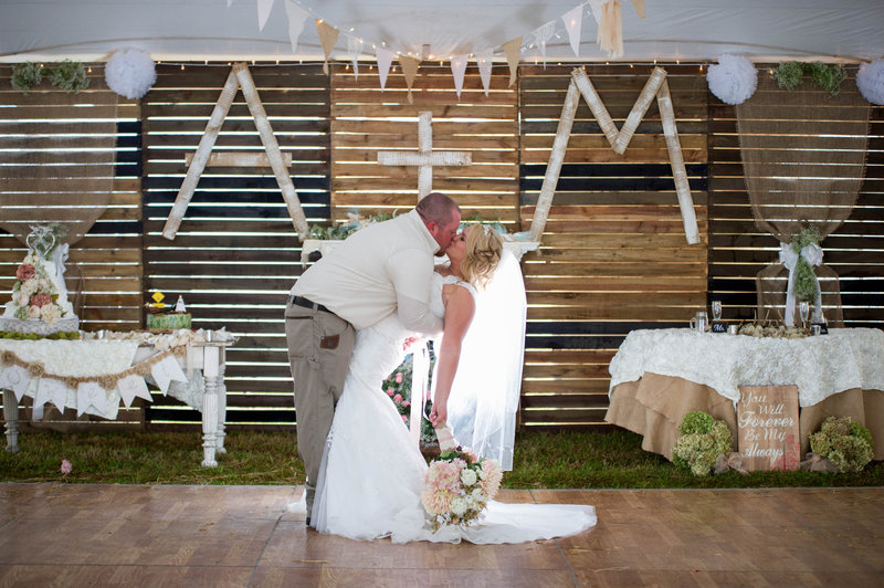 bride and groom kiss in front of DIY pallet wall