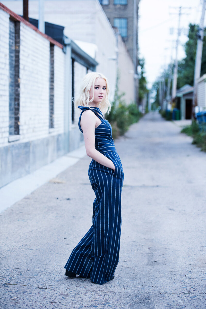 senior photo of girl in blue striped jumpsuit in alley