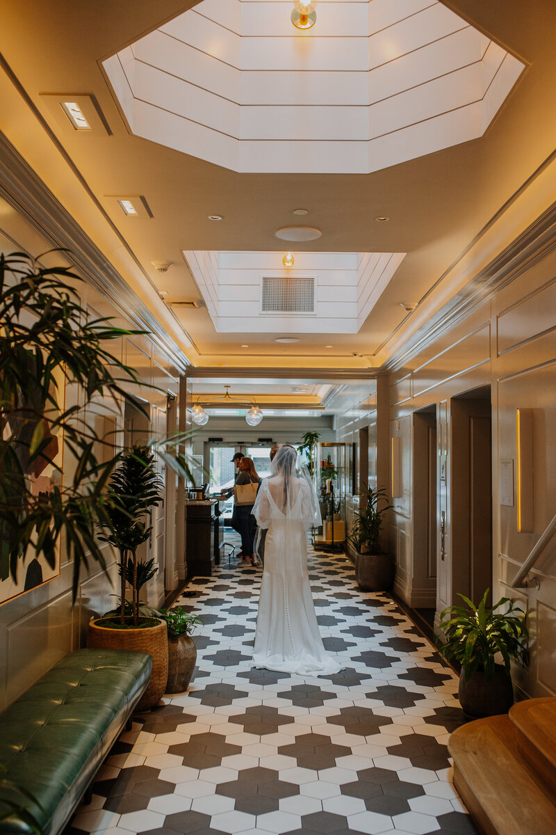 Bride in wedding dress walking through hotel lobby with skylight