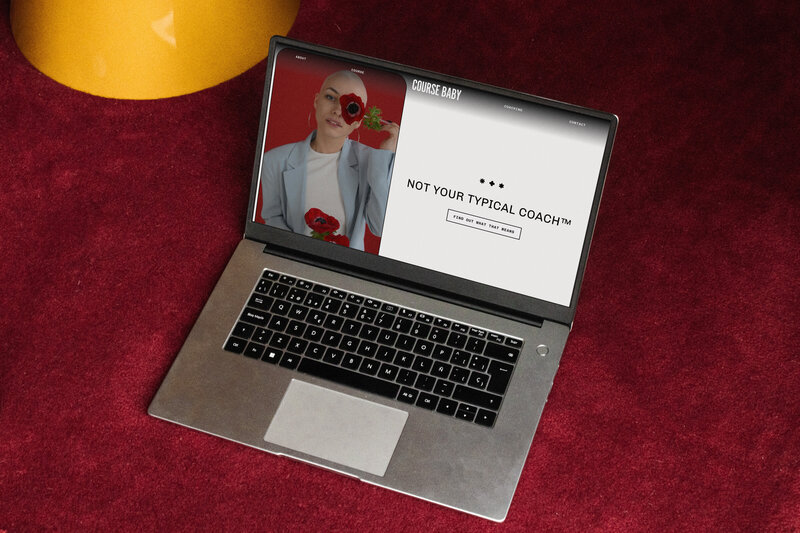 Laptop on a red carpet background showing the Course Baby website, there is a bald girl on a red background holding a flower and the text says "not your typical coach"