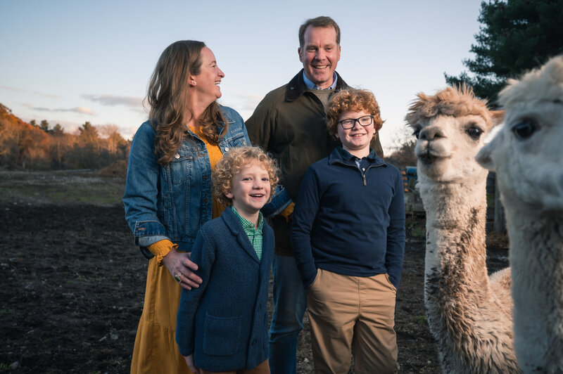 Family of 4 laughing at alpacas during a farm photo session.
