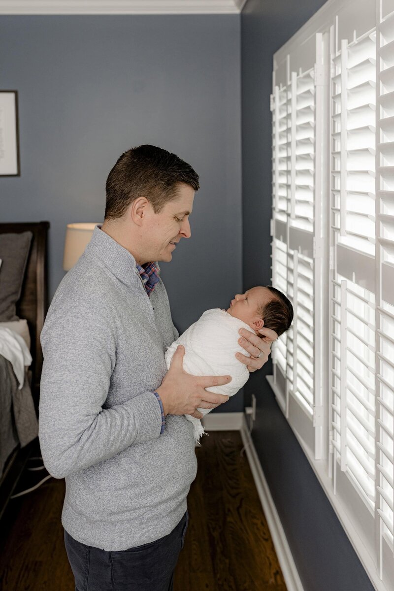 Father holds his newborn son looking down towards him in a perfect profile photo