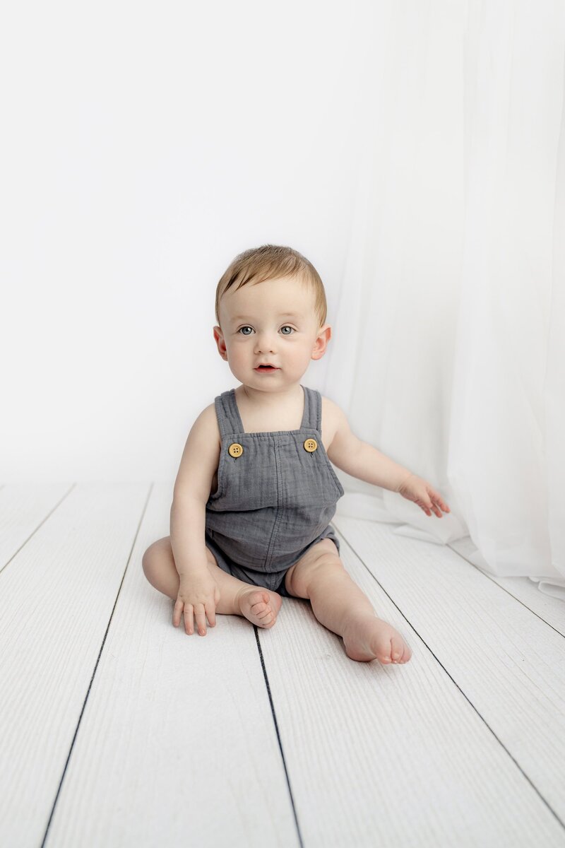 little 7 month old boy sits on white floor for his studio  sitter session