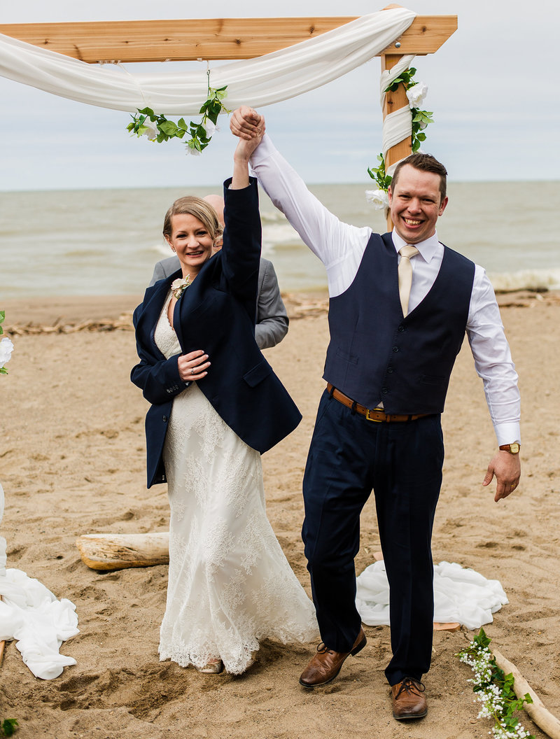 Bride and groom raise their hands after their Presque Isle beach wedding