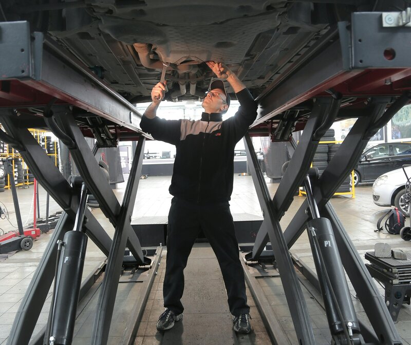 Mechanik provádí servisní kontrolu podvozku vozidla na zvedací plošině v autoservisu