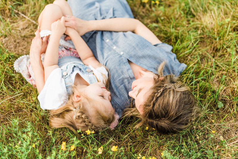 A girl and her mom lie in grass on a summer's day