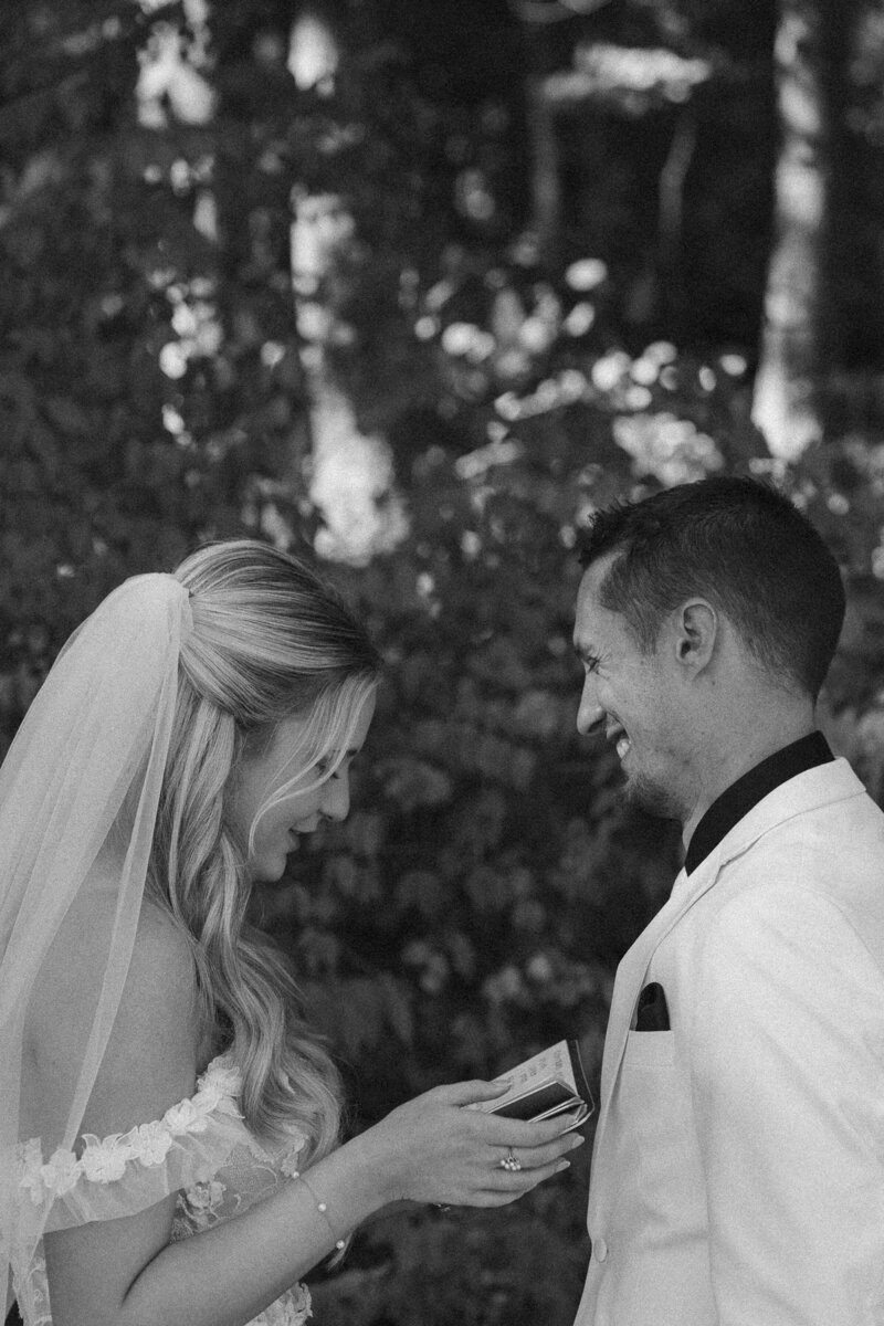 Bride smiling at groom while holding a phone in a candid black and white wedding photoshoot.