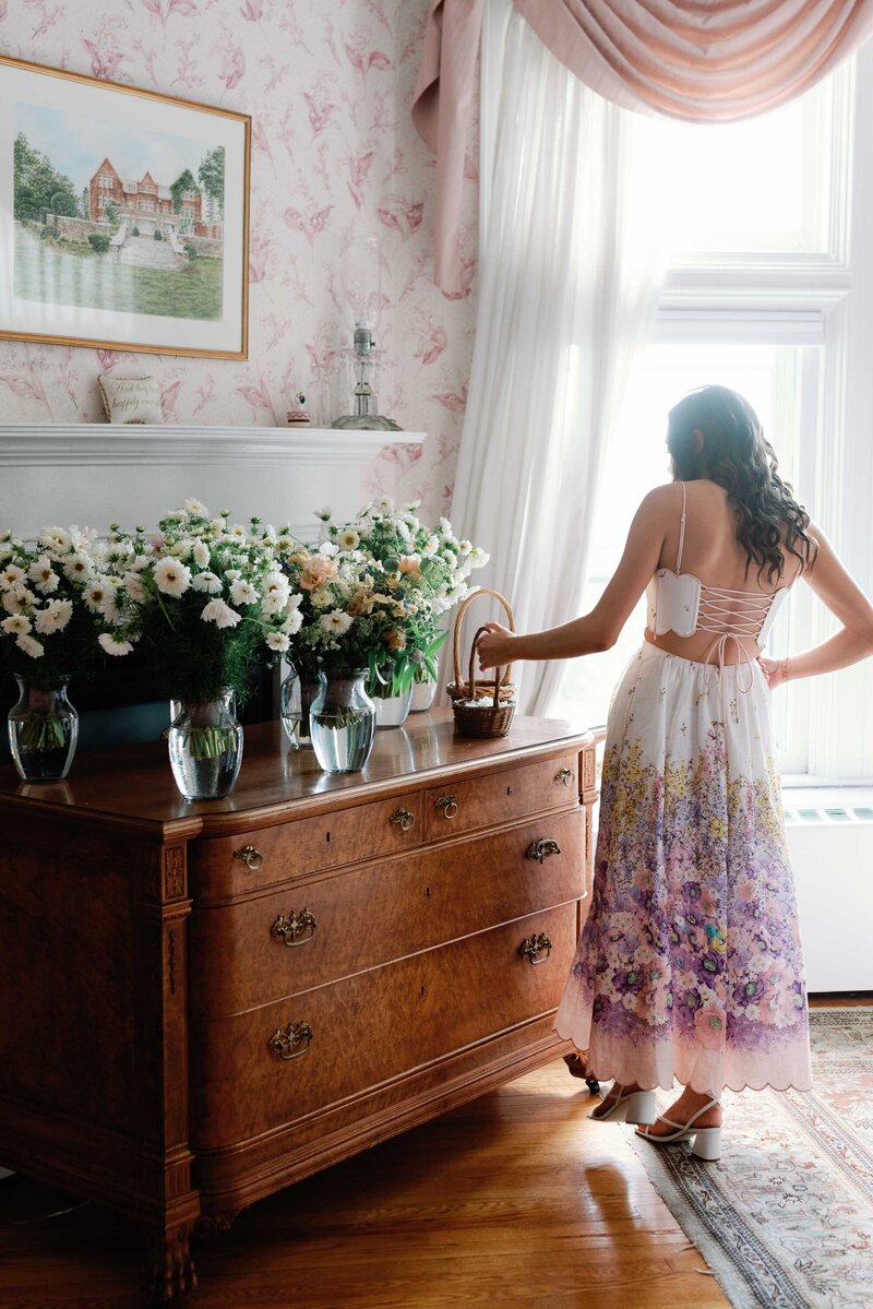 Chic bridesmaid in floral dress inspects a row of bouquets at the wilburton inn vermont wedding