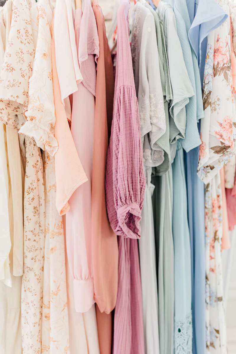 Many long flowy dresses hanging next to each other, colors and patterns ranging from neutrals to pastels