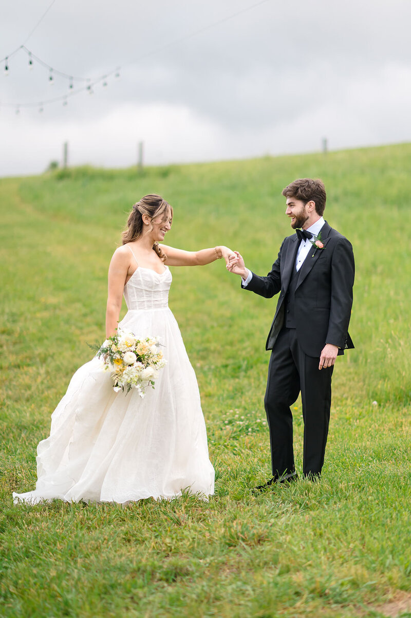 A groom holding a bride's hands while they stand in a field.
