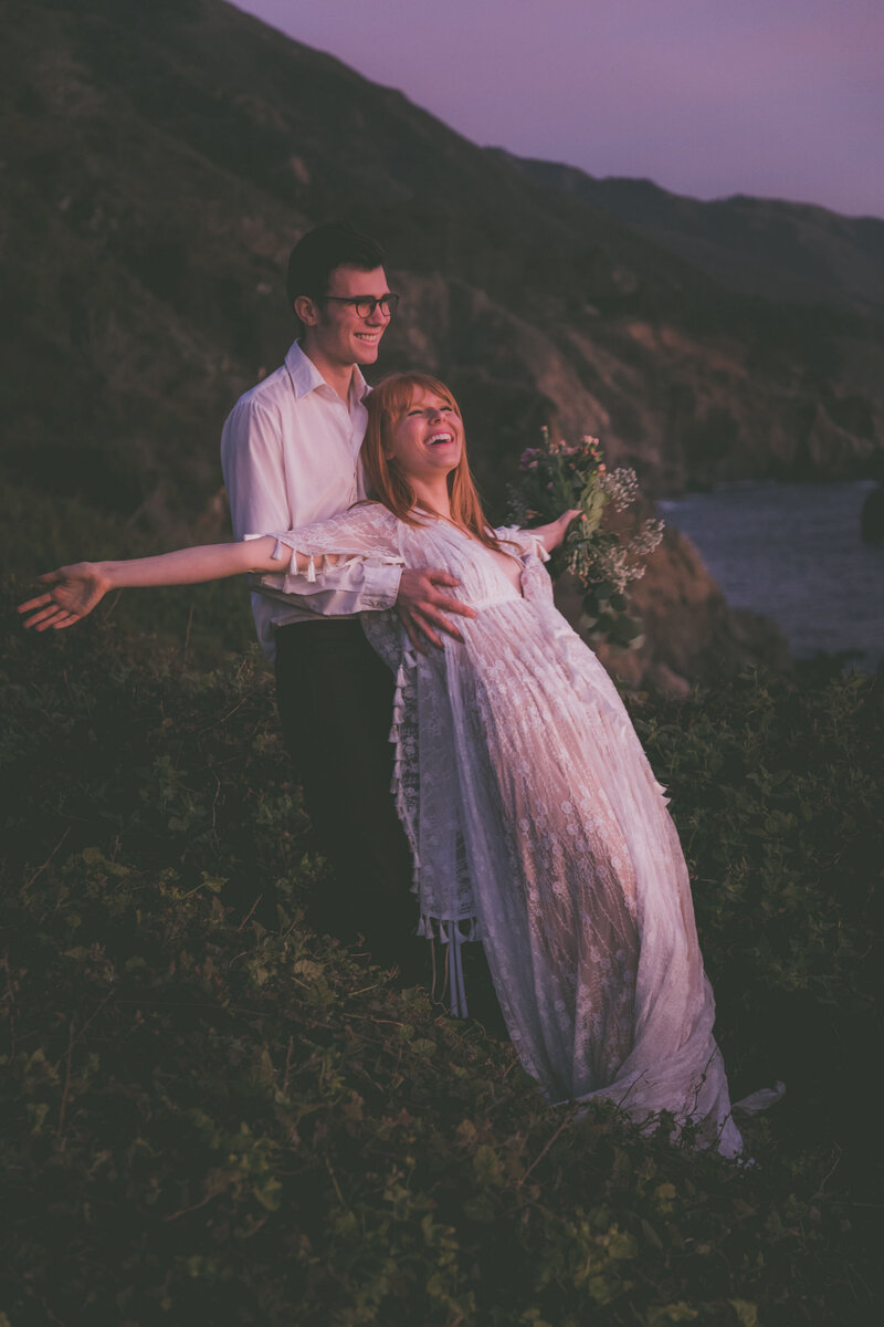 A Big Sur bride and groom do a trust fall during the pink sunset.