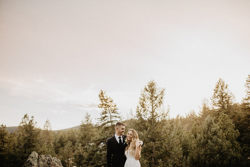 bride and groom embracing in large field with mountains in the background