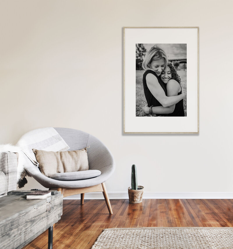 Framed photo of mother and daughter hugging on wall next to mid century modern chair